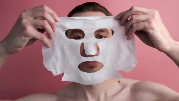 Caucasian Man Use Sheet Mask on Pink Background  the Concept of Beauty and Skin Care