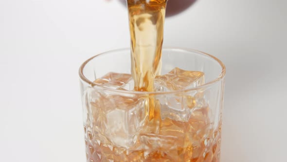 Human pours a whiskey in a glass with an ice cubes from a bottle