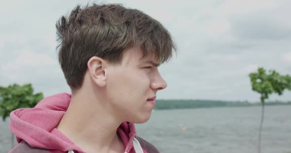 Portrait of Handsome Young Man Turns to Camera and Smiles Lightly at the Lake alt