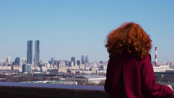 Girl with red hair standing with her back to the big city with parallax effect alt
