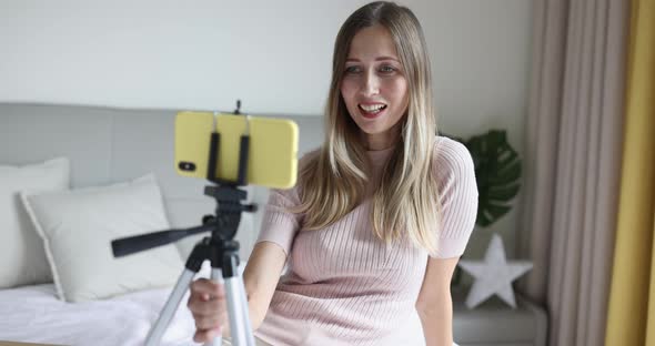 Happy Young Caucasian Woman with Blonde Hair Holding Tripod with Mobile Phone and Communicating with alt