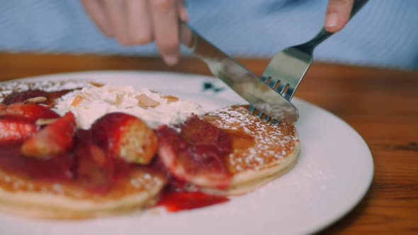 Cutting pancake on plates. Woman sitting inside a cafe.