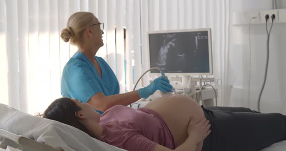 Senior Doctor Doing Ultrasound Scan for Young Pregnant Woman in Hospital alt