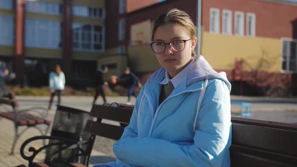 A Teenage Girl is Sitting on a Bench on Campus Looking Back at Teenagers Playing Basketball in the alt