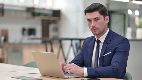 Businessman Working on Laptop Pointing at the Camera in Office  alt
