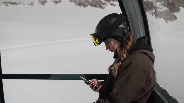 Woman In Skiwear Looking Up From Phone In Cable Car alt
