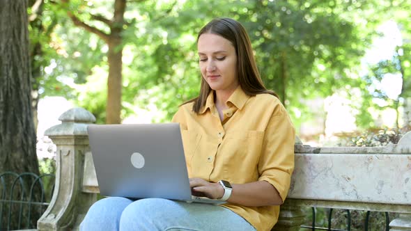 Optimistic Young Woman Using Laptop Sitting on the Bench in Campus Area