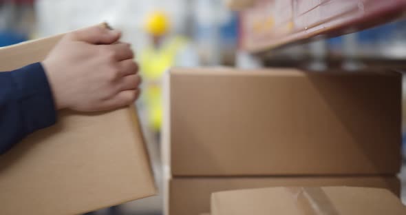 Close Up of Warehouse Worker Putting Cardboard Box on Shelf alt