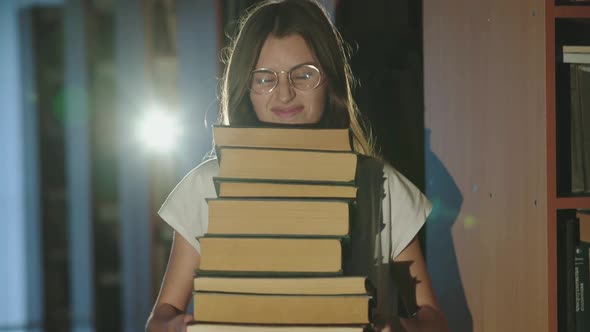 Cheerful Female Student Holds Stack of Books in Her Hands and Laughs in Library alt