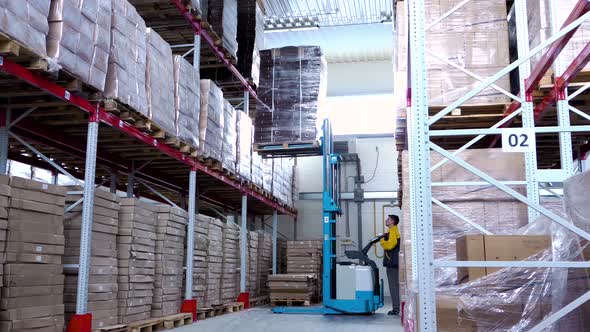 Warehouse Worker Driver in Uniform Loading Cardboard Boxes By Forklift Stacker Loader