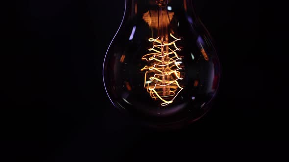 A vintage decorative light bulb shines in the dark close up.