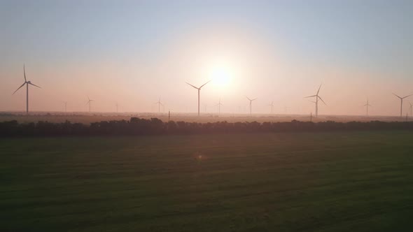 Windmills with rotating wings at sunset or sunrise.