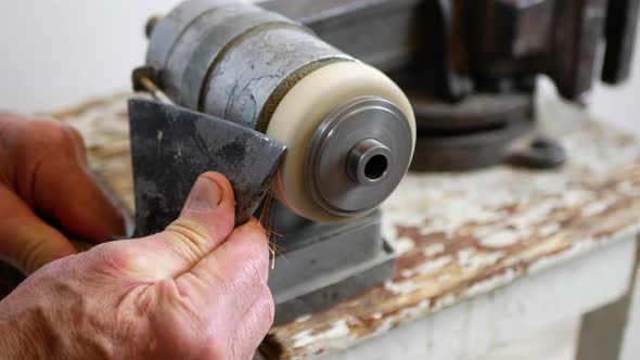 Man is sharpening the axe using grinding machine, sparks are flying