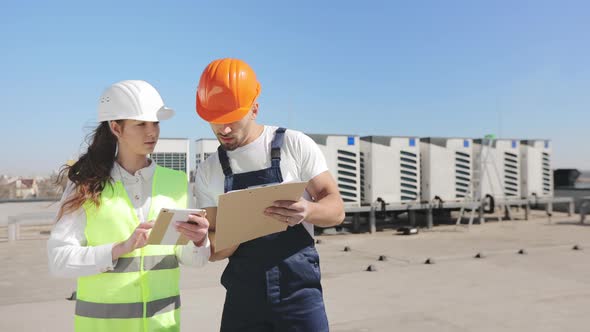 Two Happy Engineers are Discussing Works Documents and Making Notes alt