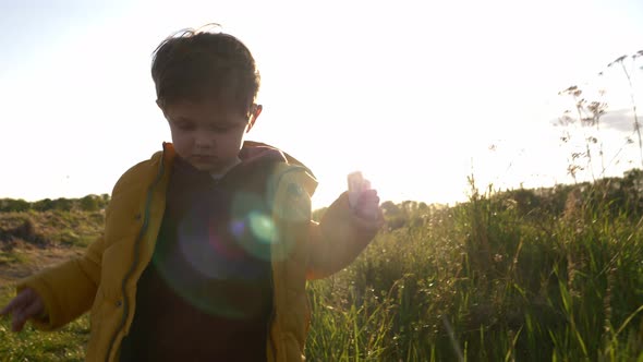 Little boy in yellow jacket play with grass in countryside