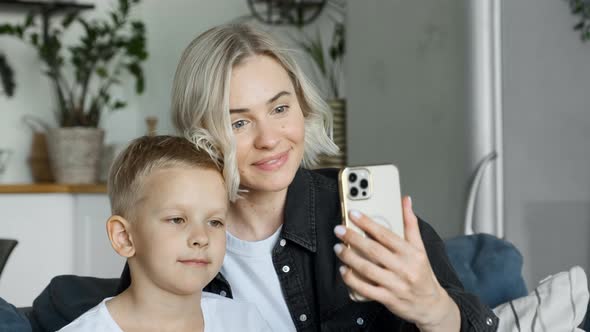Pretty girl mother is taking selfie with cute son laughing and having fun holding smartphone alt