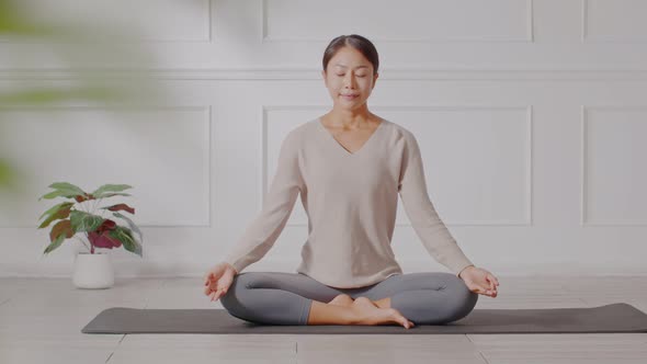 Calm of wellness Asian young woman sit on carpet breathing with yoga lotus pose alt