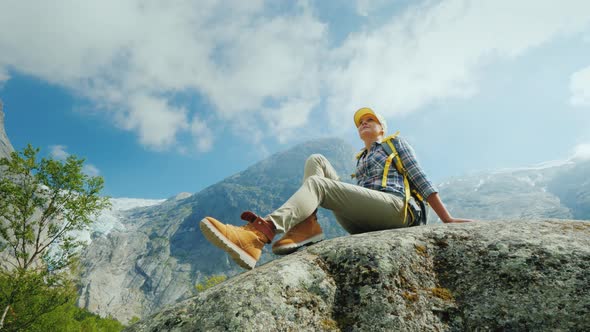 An Active Woman with a Backpack Sits on a Huge Stone alt