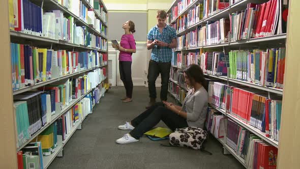 Group of students in library reading and playing with mobile phone alt