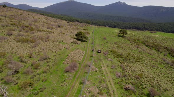 Aerial following flight behind buggy car driving in wilderness of Spain with mountain range silhouet alt