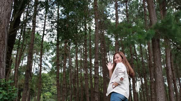 A female traveler walking and waving hand in the pine tree woods