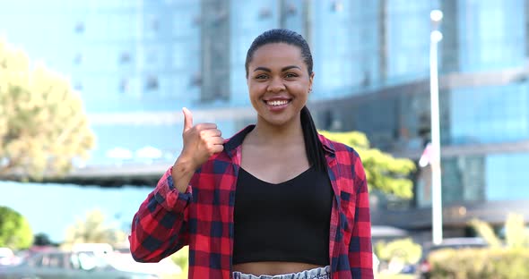 African woman standing outdoors smiling white healthy toothy smile looks at camera showing thumbs up alt