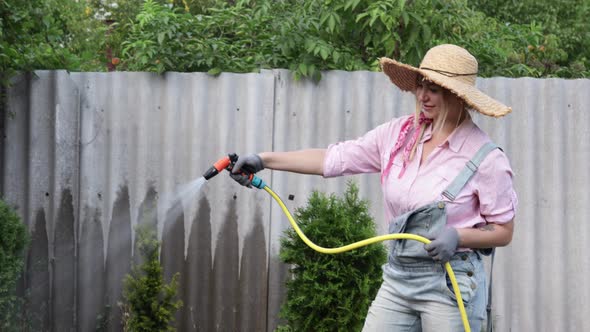 A Young Adult Woman Wateres a Vegetable Garden with a Garden Hose Outside the House alt