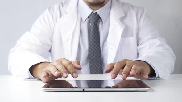 The doctor sat at the table typing data on the tablet for the treatment of patients. alt