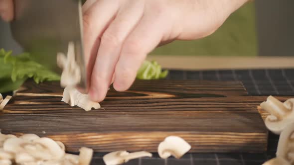 the Male Hands of the Cook Cut Fresh Champignon Mushrooms on a Wooden Brown Board with the Help of a