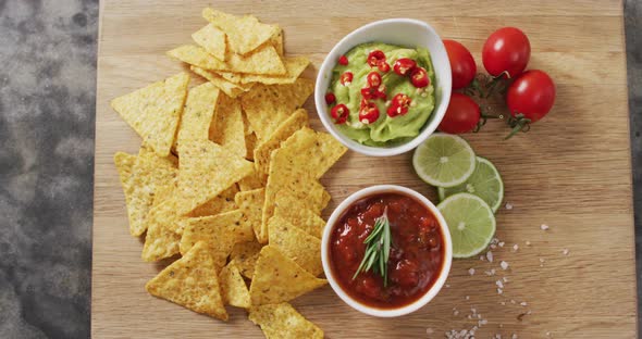 Close up of nachos and sauces on wooden tray on black surface alt