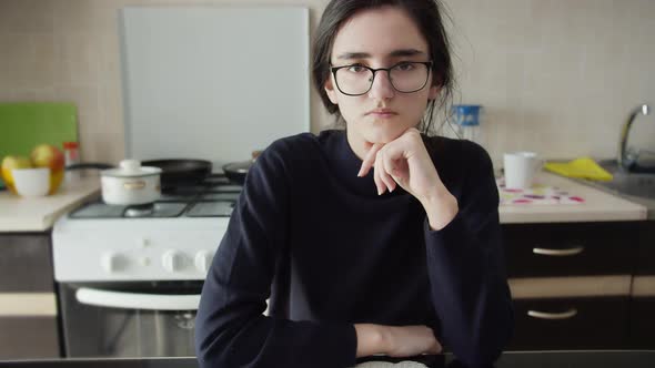 Portrait of a Serious Girl Sitting in the Kitchen and Looking at the Camera