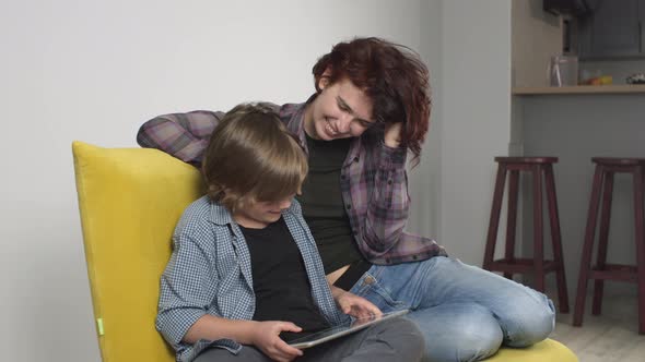 Slow Motion Happy Young Mother Watching Son Kid Playing Digital Tablet Video Game Smiling and