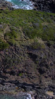 Aerial Vertical Flyover Along Jagged Rocks with Waves Crashing the Shore