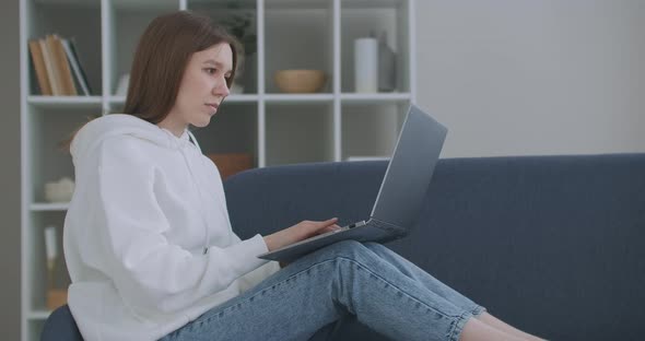Woman Using Laptop on Couch at Home, Thoughtful Young Woman Sitting with Computer on Couch, Looking alt