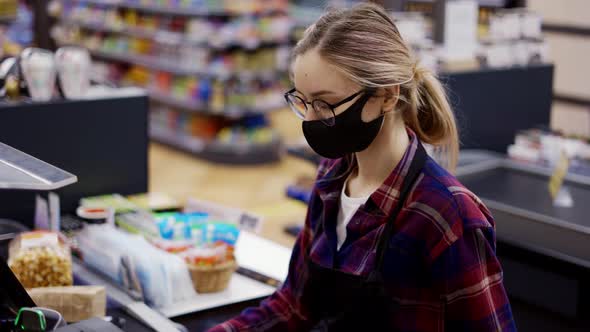 Female Cashier in a Protective Mask Pierces the Products with the Scanner alt