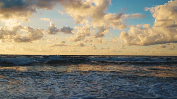 Sunset behind Clouds over Sea Waves and Sandy Beach alt