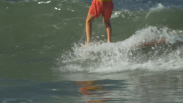 A male surfer riding a wave and doing a hang-5 trick on a longboard surfboard. alt