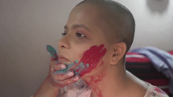 Bald Cancer patient Indian girl smiles and applies color powder on cheeks on Holi, Indian festival a alt