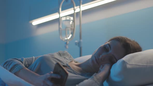 Young patient lying in bed at the hospital and using her smartphone