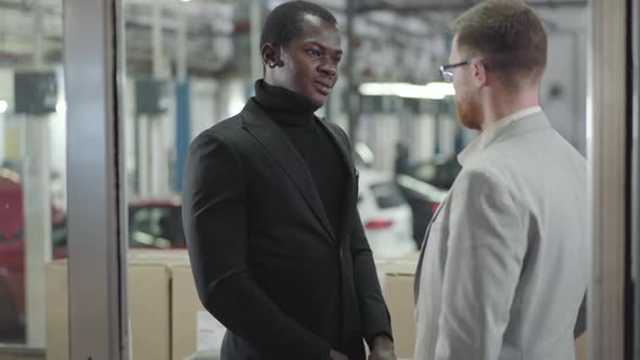 Young Cheerful African Americam Car Dealer Giving Keys To Successful Caucasian Redhead Man in alt