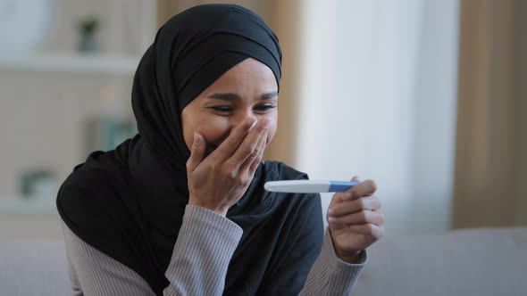 Portrait Joyful Surprised Girl in Hijab Holding Pregnancy Test Sit in Living Room Excited with alt