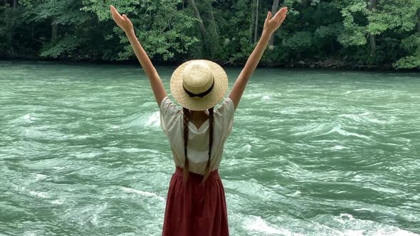 Young beautiful vintage woman in straw boater hat raising hands up near mountain river travel nature alt