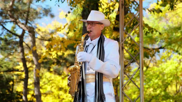 Senior Man with Saxophone Performs on Stage in Autumn Park