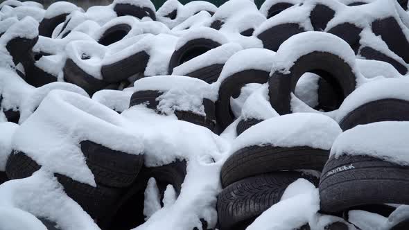 Stack of used car tires covered with snow on a landfill. Environment disaster concept.