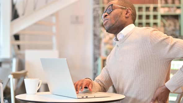 Hardworking African Man with Laptop Having Back Pain in Cafe alt