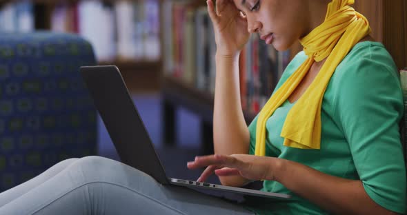 Asian female student wearing a yellow hijab sitting and using laptop alt