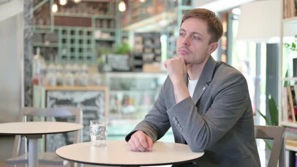 Young Man Sitting in Cafe Thinking alt