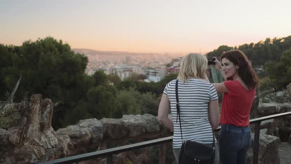 Young adult women admiring view and take picture on mobile phone in Barcelona