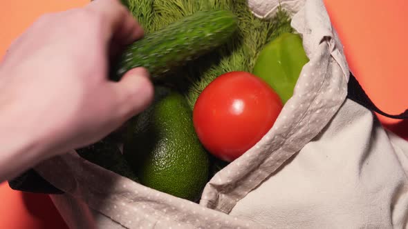 A Man Puts Vegetables in a Cotton Bag on an Isolated Colored Background. Cucumbers, Tomatoes