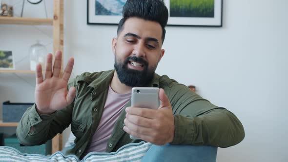 Cheerful Middle Eastern Guy Making Online Video Call Waving Hand and Talking Using Smartphone at alt
